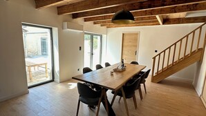A dining area with a wooden table and chairs, a black pendant light, and a wooden staircase. - Gîte de Condeiss (Condeissiat)