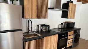 A modern kitchen with wooden cabinetry, stainless steel appliances, and a black countertop. - Gîte de Condeiss (Condeissiat)