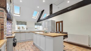 A modern kitchen with white cabinets, a wooden countertop, and a brick wall. There are skylights, a radiator, and a window.