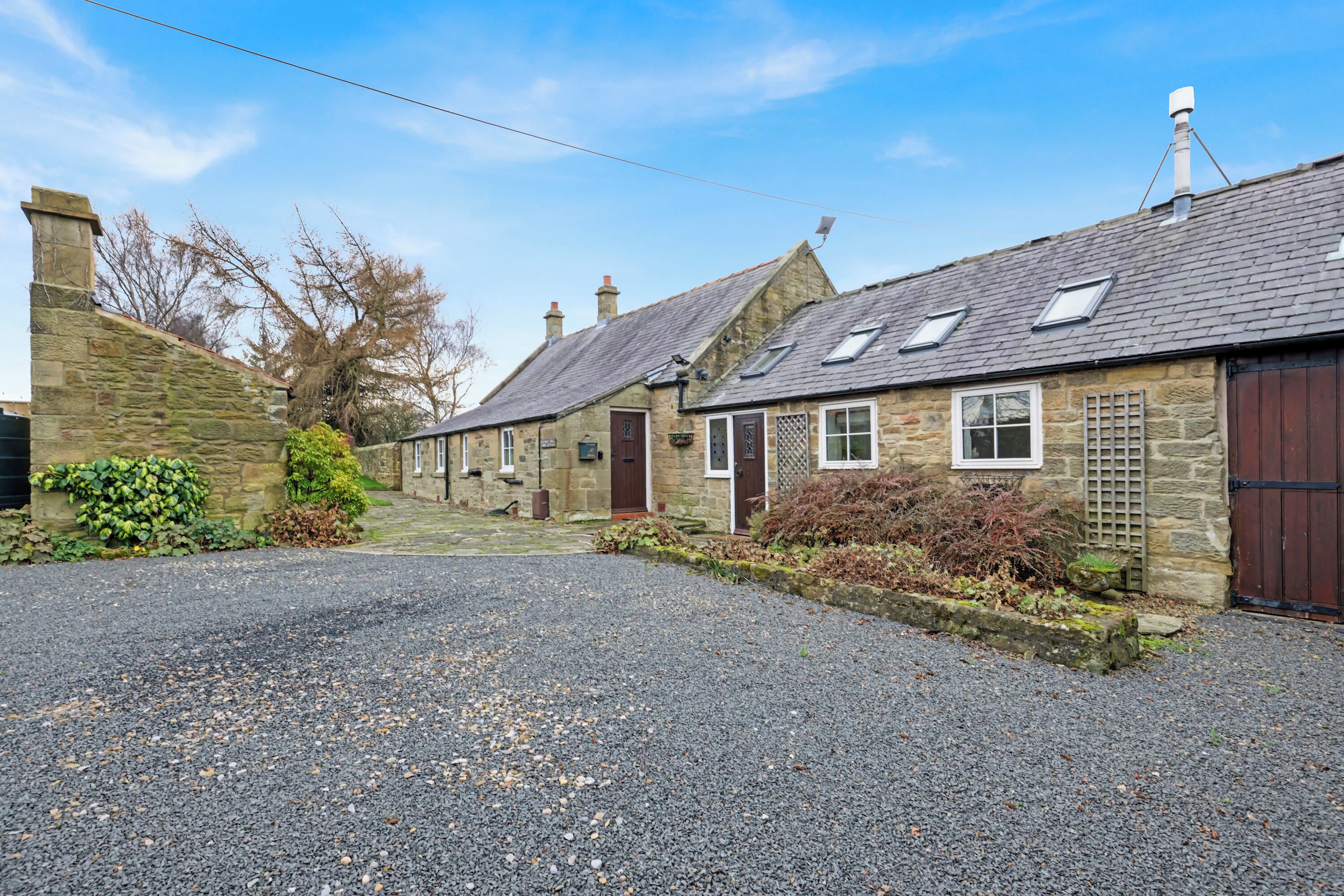 A stone building with a gravel driveway and a small garden area.