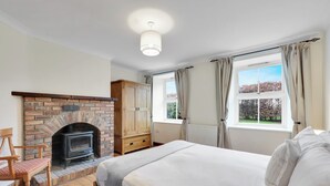 A bedroom with a brick fireplace, a bed, a wooden chair, and a window with curtains.