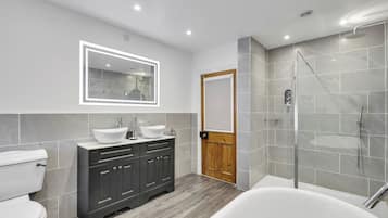 A modern bathroom with a white toilet, dark wooden cabinets, a large mirror with LED lighting, a white sink, and a walk-in shower.