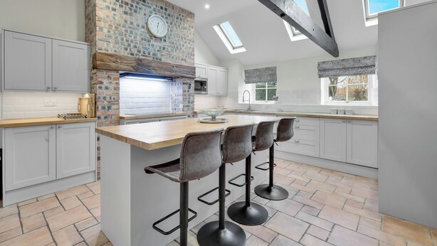 A modern kitchen with a brick wall, a clock, and a skylight.