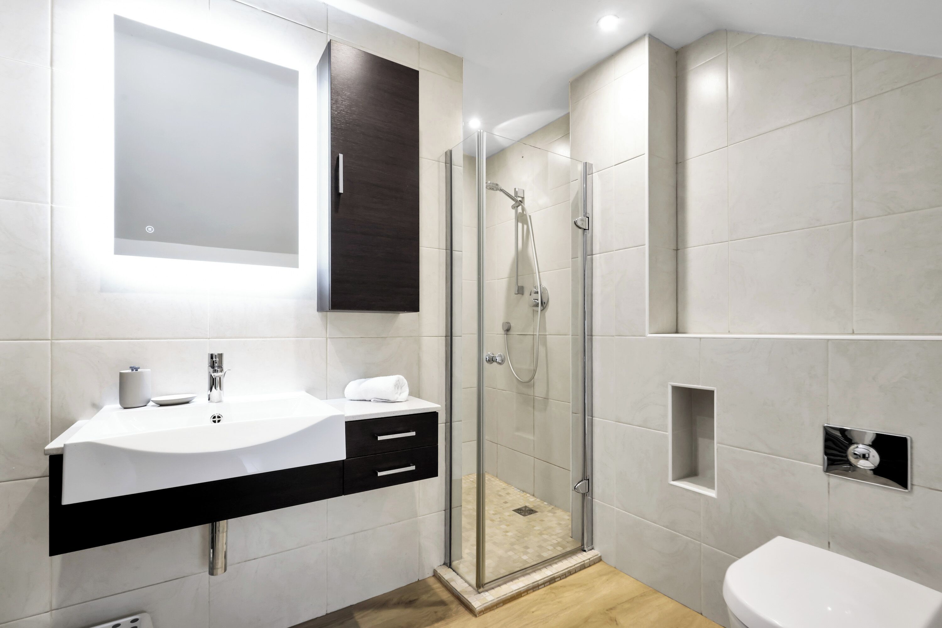 A modern bathroom with a glass-enclosed shower, a white sink with a dark countertop, and a large mirror above the sink.
