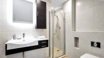 Een moderne badkamer met een douchecabine van glas, een wit wastafelmeubel met een donker aanrechtblad en een grote spiegel erboven.