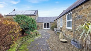 A stone house with a tiled patio, a small tree, and a bench.