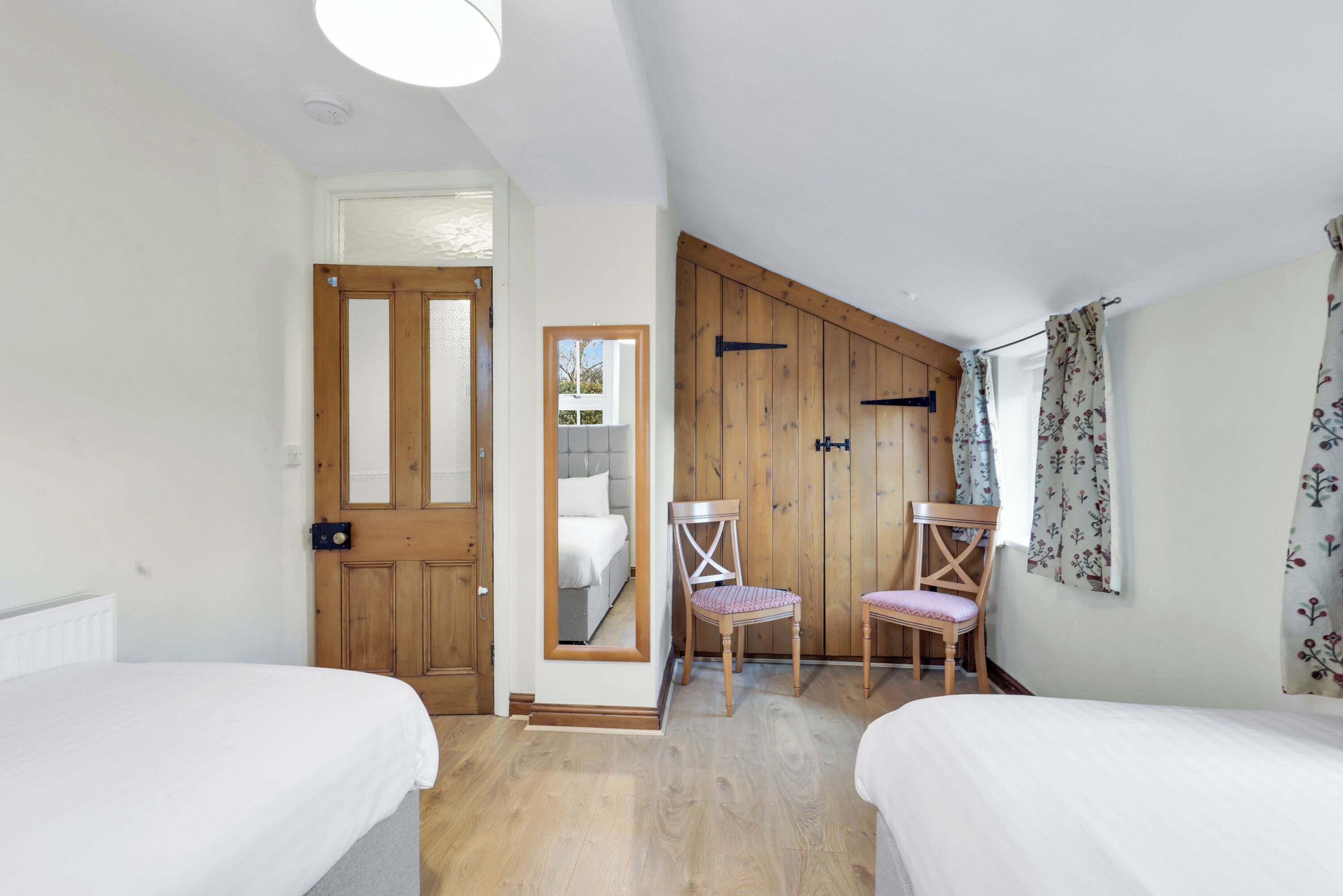 A bedroom with two beds, wooden walls, a mirror, and a chair.