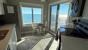 Une cuisine moderne avec vue sur l’océan, un coin repas avec une table et des chaises, et une grande porte-fenêtre coulissante donnant sur un balcon.