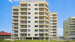 Un hôtel à plusieurs étages, doté de balcons à chaque niveau, d’un toit plat et, en arrière-plan, d’un ciel bleu dégagé.