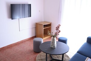Uma sala de estar moderna com uma televisão de tela plana na parede, um armário de madeira, uma mesa redonda com um vaso de flores e um sofá azul.