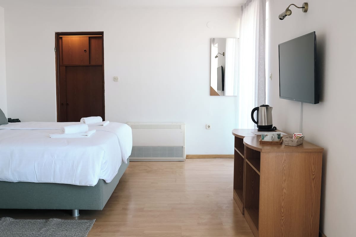 Une chambre d’hôtel moderne équipée d’un lit, d’une armoire en bois, d’un téléviseur à écran plat et d’un miroir.