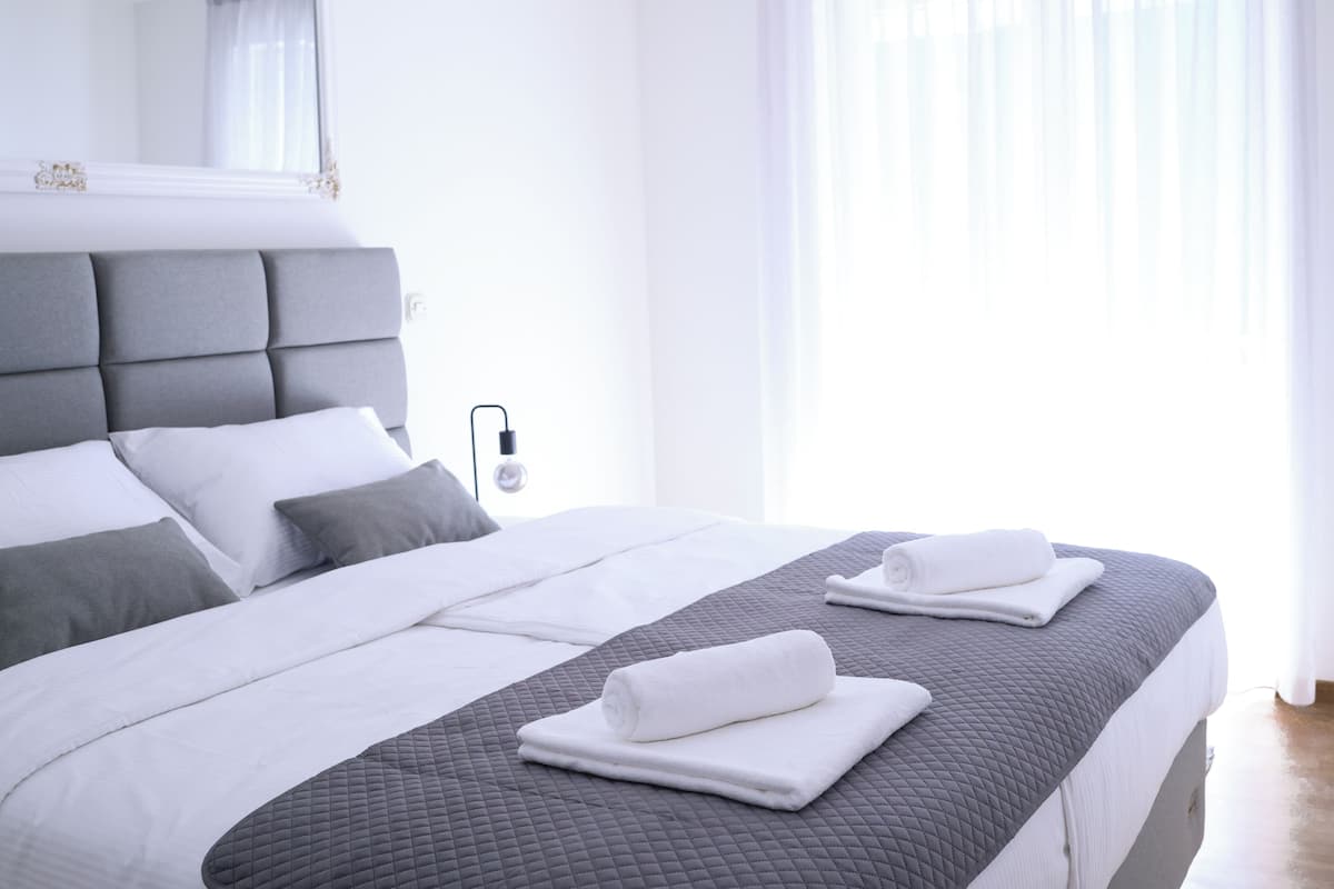 Une chambre d’hôtel moderne avec un grand lit, une literie aux tons de gris et de blanc, et une lampe de chevet.