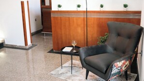 Eine moderne Lobby mit Ledersessel, Stehlampe, kleinem Tisch mit einem Weinglas und einer Wanddekoration.