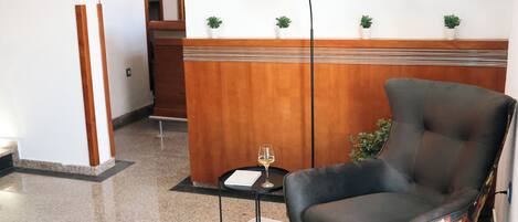 Un vestíbulo moderno con un sillón de cuero, una lámpara de pie, una mesita con una copa de vino y un adorno en la pared.