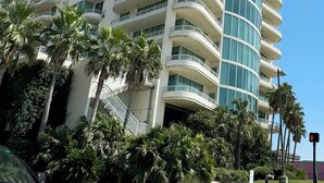 A high-rise hotel with multiple balconies, a curved glass facade, and palm trees in the foreground. - Beautiful Sunset and Gulf Views-2 bedroom / 2 bathroom (Biloxi)