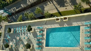 An aerial view of a rooftop swimming pool with multiple lounge chairs and small potted plants. - Beautiful Sunset and Gulf Views-2 bedroom / 2 bathroom (Biloxi)