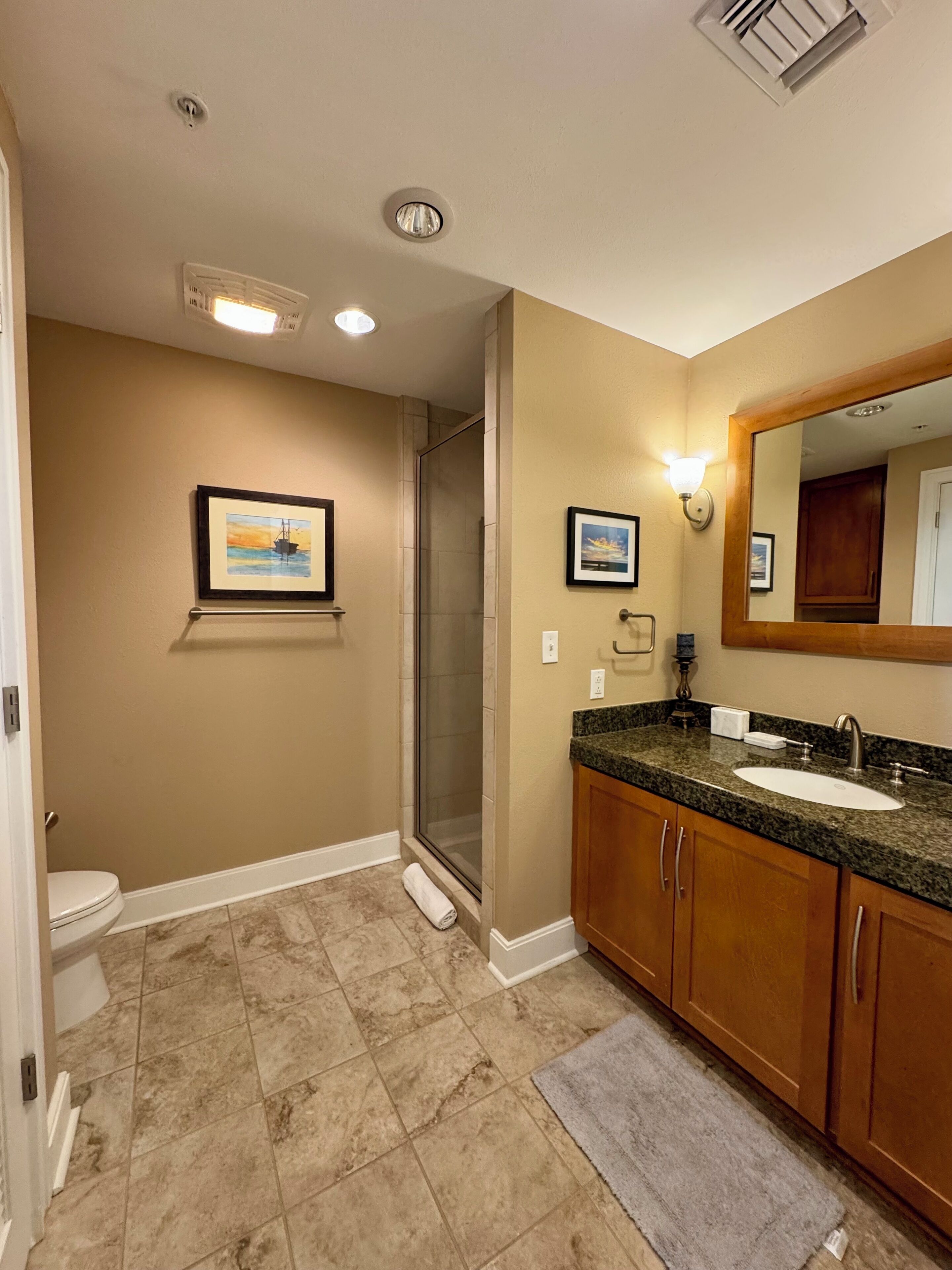 A bathroom with a shower, toilet, sink, and framed pictures on the wall.