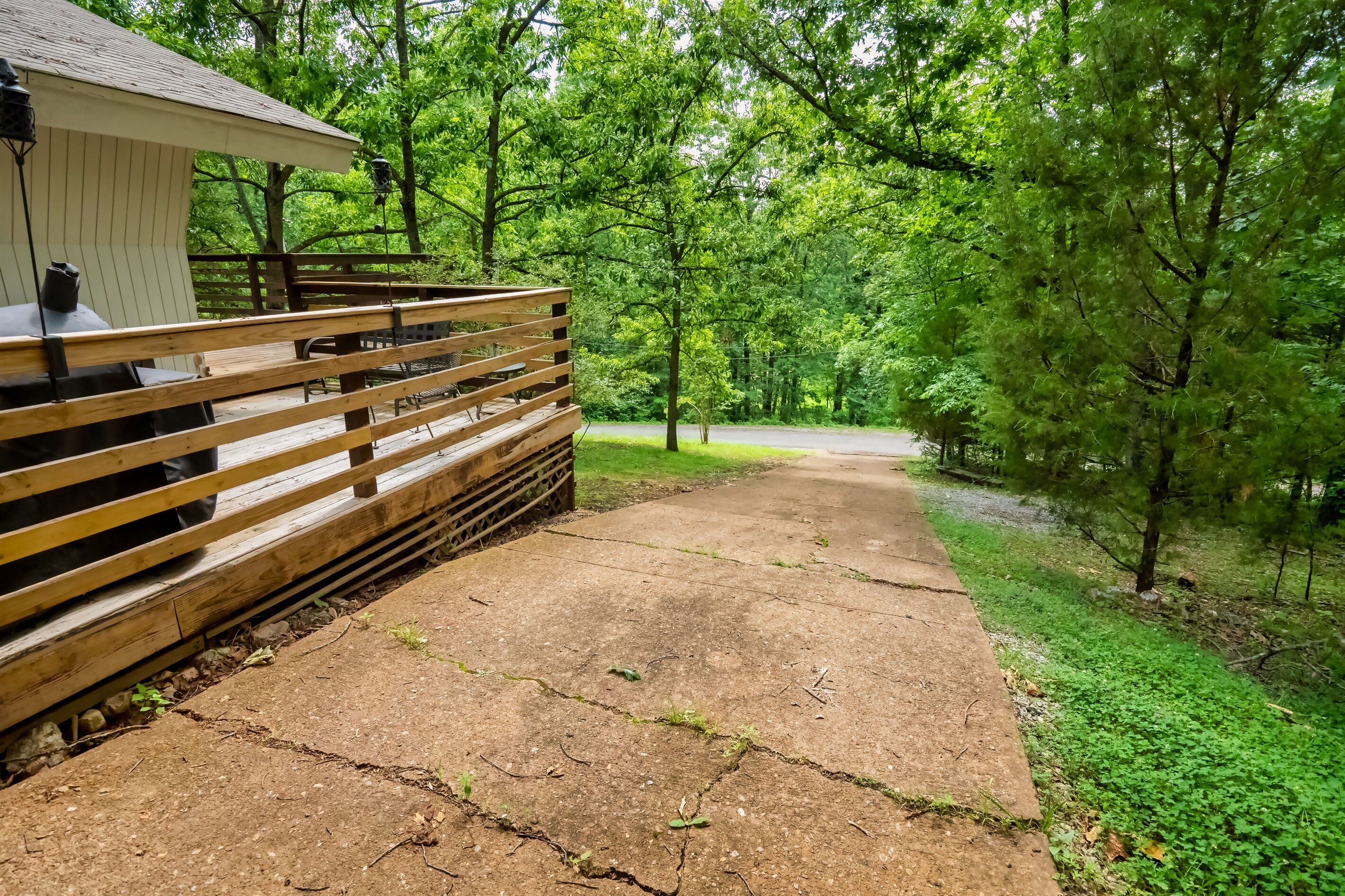 A wooden deck with a grill and outdoor seating, surrounded by lush greenery and trees.