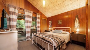 Un dormitorio con cama, mesitas de noche, escritorio y ventana con cortinas.
