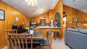 Una cocina compacta con paredes de madera, una zona de comedor con mesa y sillas, y un sofá gris en la sala.
