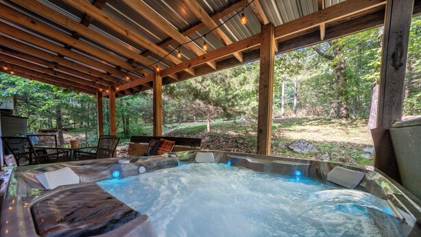 Un jacuzzi con una pérgola de madera sobre él, rodeado por un entorno natural de bosque.