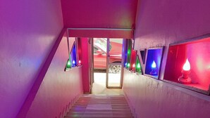 A staircase with colorful lighting fixtures on the walls and a red car visible through the open door at the top. - Nairobi Fahari Tripple Suites (Nairobi)