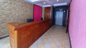 A reception area with a wooden counter, a stone wall, a red door, and a blue door. - Nairobi Fahari Tripple Suites (Nairobi)