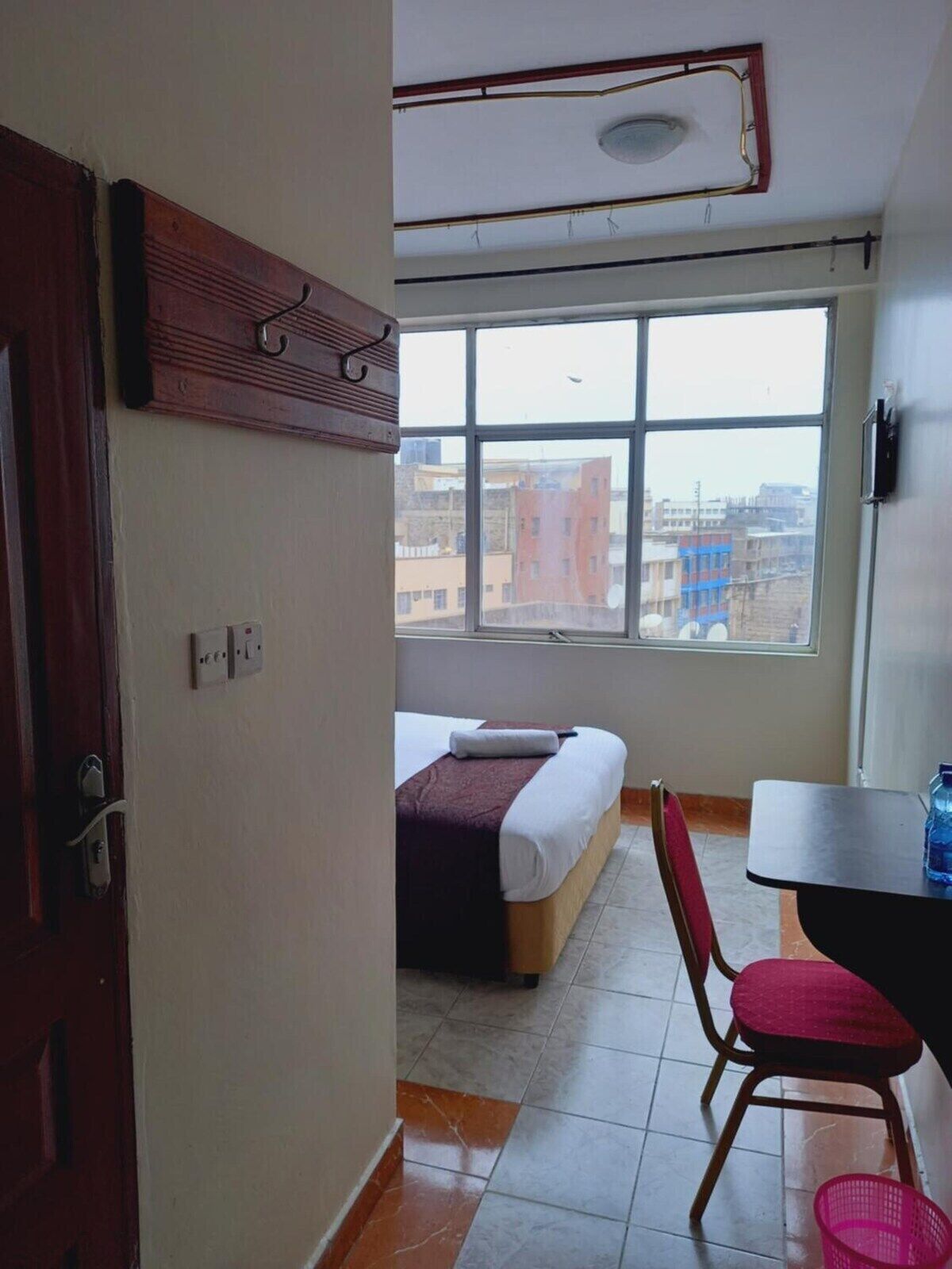 Ein Zimmer mit Bett, Stuhl, Tisch und Fenster mit Blick auf die Stadt.