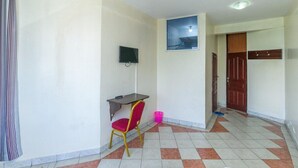 A hallway with a tiled floor, a desk with a chair, a television mounted on the wall, and a door. - Nairobi Fahari Tripple Suites (Nairobi)