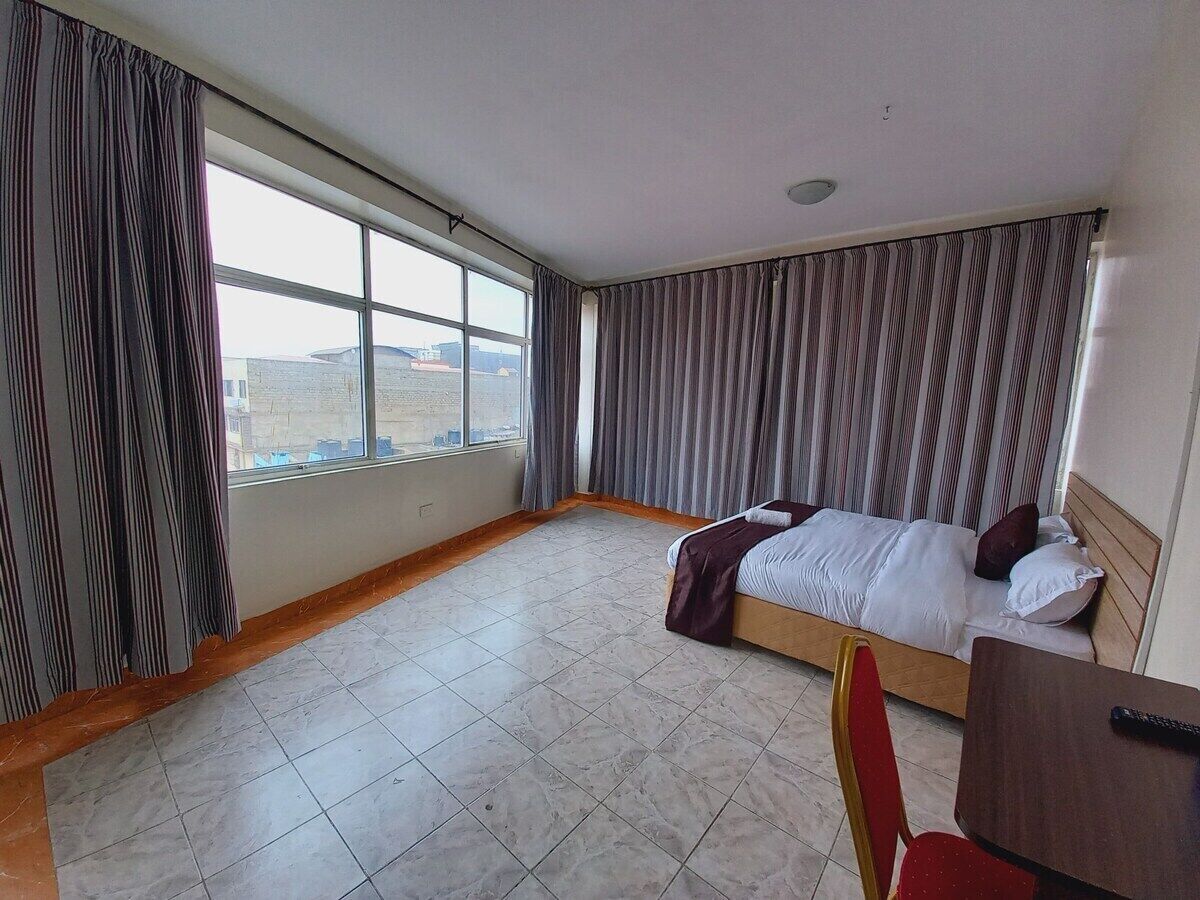 A hotel room with a bed, a desk, and a view of the city.