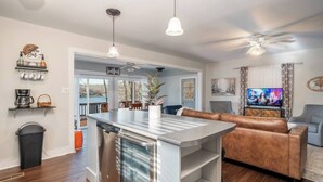 Una cocina moderna con una isla central, un comedor con un sofá de cuero marrón y una sala de estar con televisor.