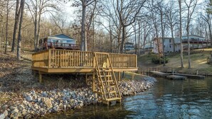 Una terraza de madera con una escalera que lleva a una casa junto a un río.
