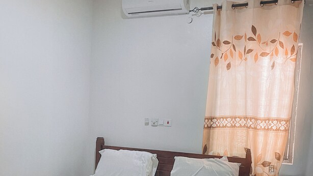 A bedroom with a bed, a nightstand, an air conditioner, and a curtain. - ZOHZEE GUEST HOUSE (Tema)