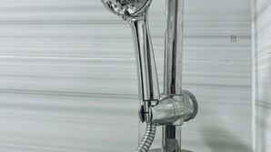 A chrome showerhead with a flexible hose, mounted on a wall with a control panel. - ZOHZEE GUEST HOUSE (Tema)