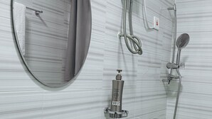 A modern bathroom with a round mirror, a handheld showerhead, a handheld showerhead with a circular head, a handheld showerhead with a long hose, and a sink with a faucet. - ZOHZEE GUEST HOUSE (Tema)