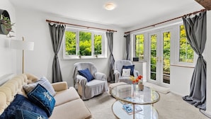 A living room with a sofa, two armchairs, a glass coffee table, and large windows with curtains.