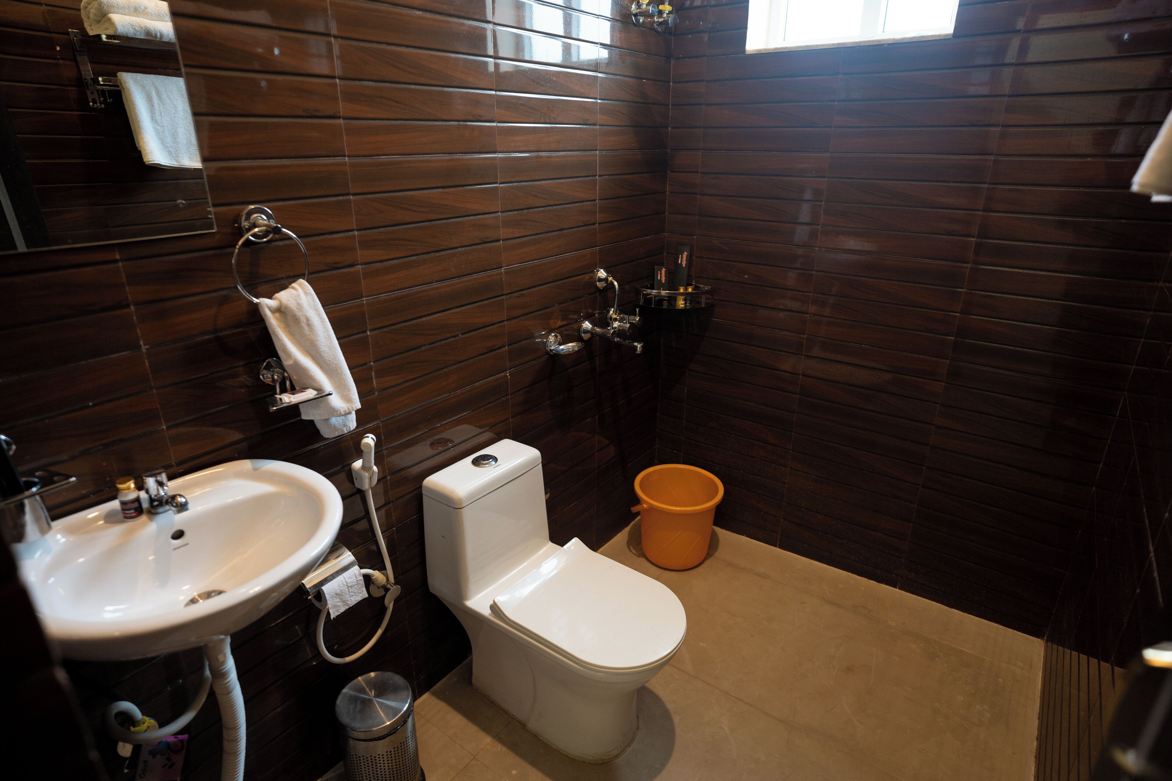 A bathroom with a white sink, toilet, and orange bucket.