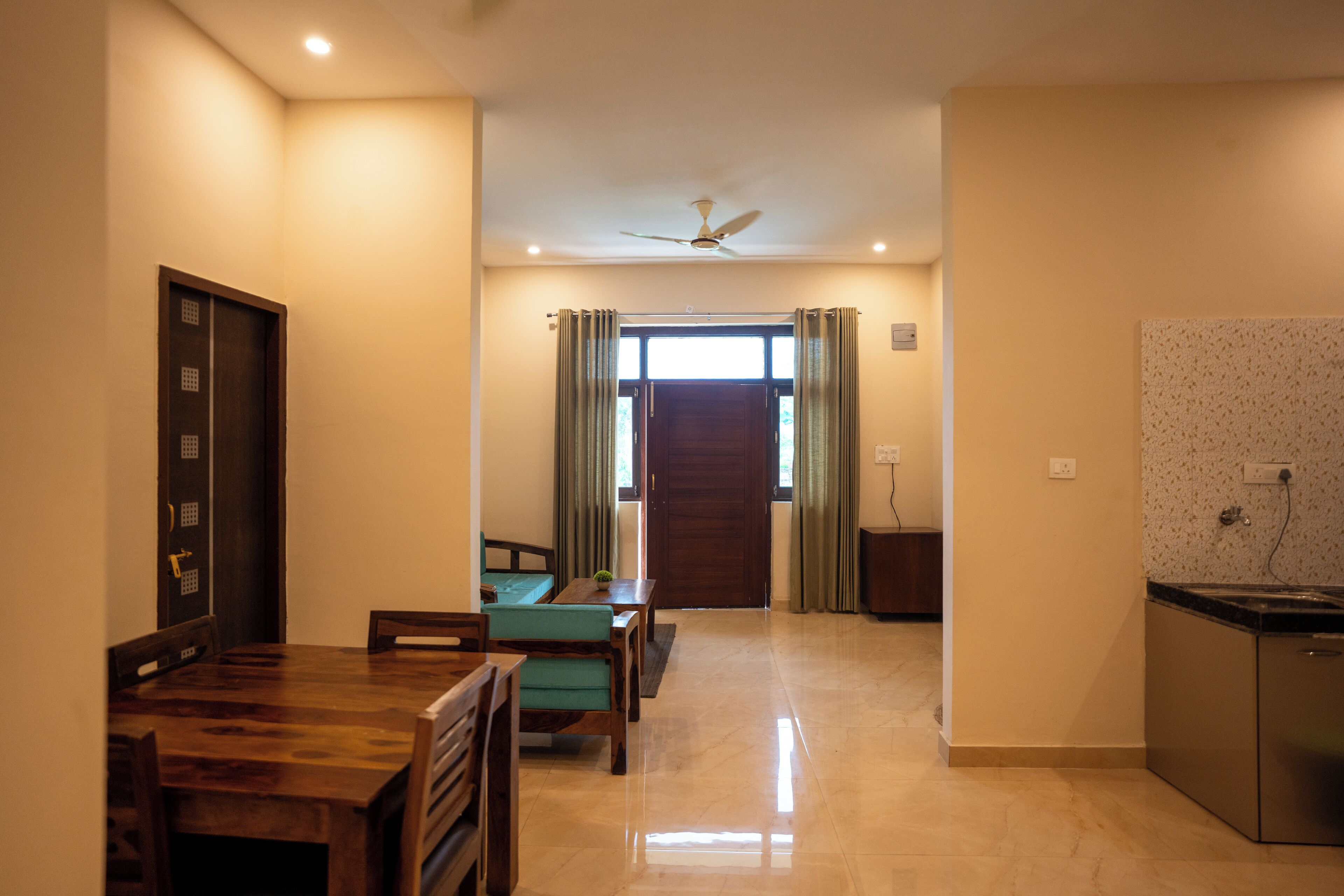 A spacious living area with a wooden dining table, chairs, a sofa, a ceiling fan, and a kitchen area with a dishwasher.