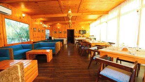A wooden interior with a sofa, tables, and chairs, a television, and large windows. - Aanandam Resort and Spa Pushkar (Pushkar)