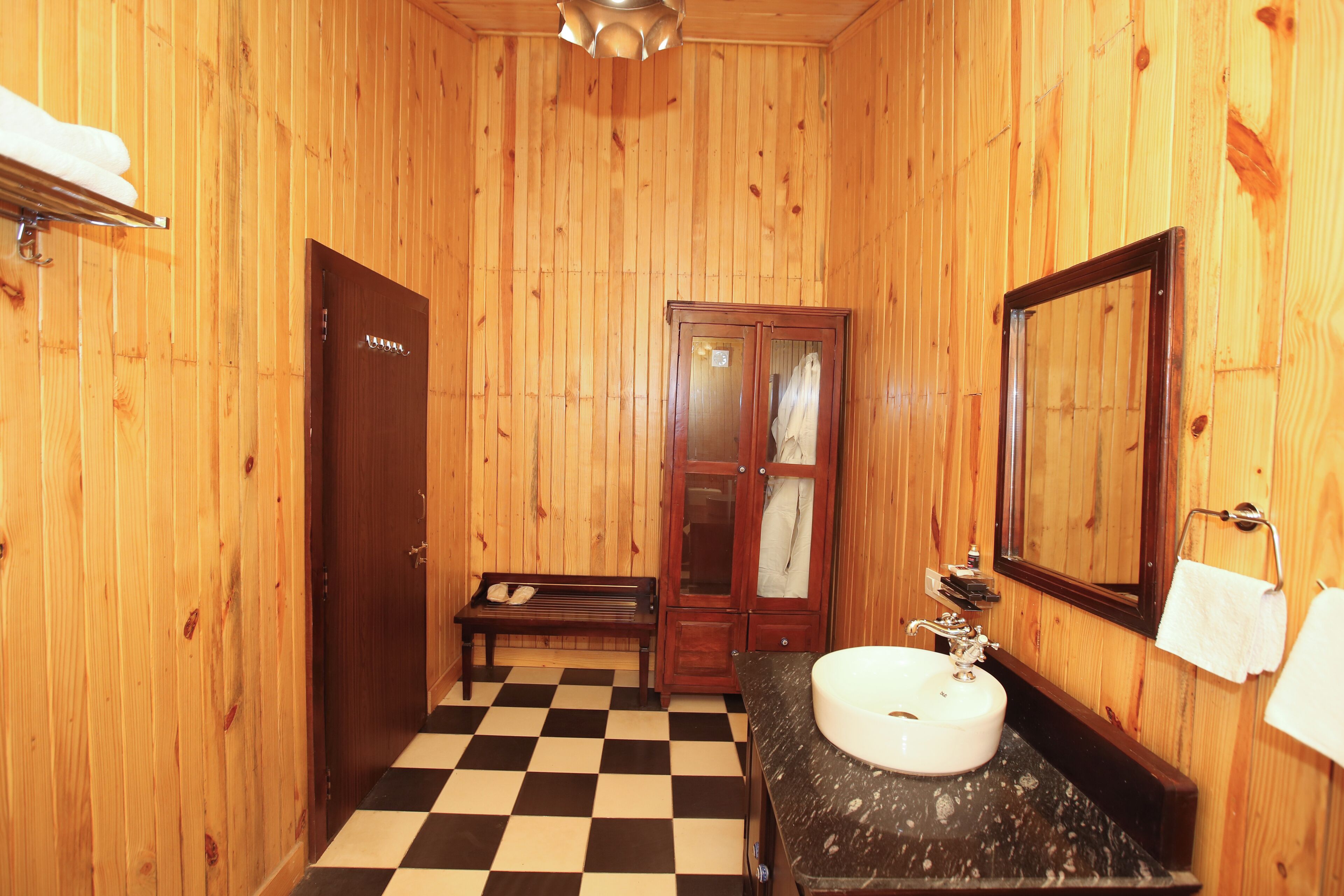 A wooden-paneled bathroom with a checkered floor, a sink, a mirror, and a bench.