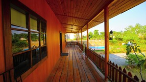 A wooden covered porch with a view of a pool and greenery. - Aanandam Resort and Spa Pushkar (Pushkar)