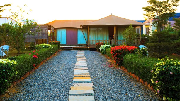 A pathway leading to a house with a porch, surrounded by well-maintained hedges and colorful flowers. - Aanandam Resort and Spa Pushkar (Pushkar)