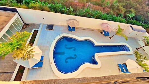 Ein Pool mit ungewöhnlicher Form, umgeben von einer Liegefläche mit Liegestühlen und Sonnenschirmen.