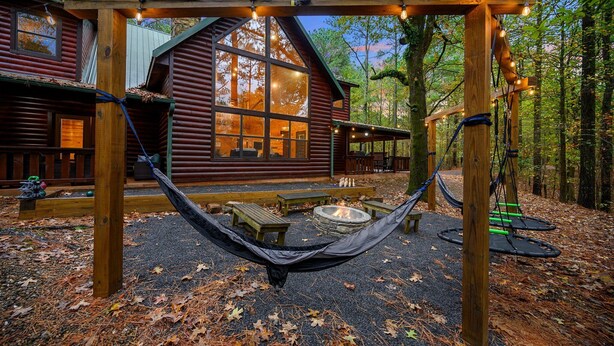 Une cabane en bois avec un hamac, un foyer et une terrasse.