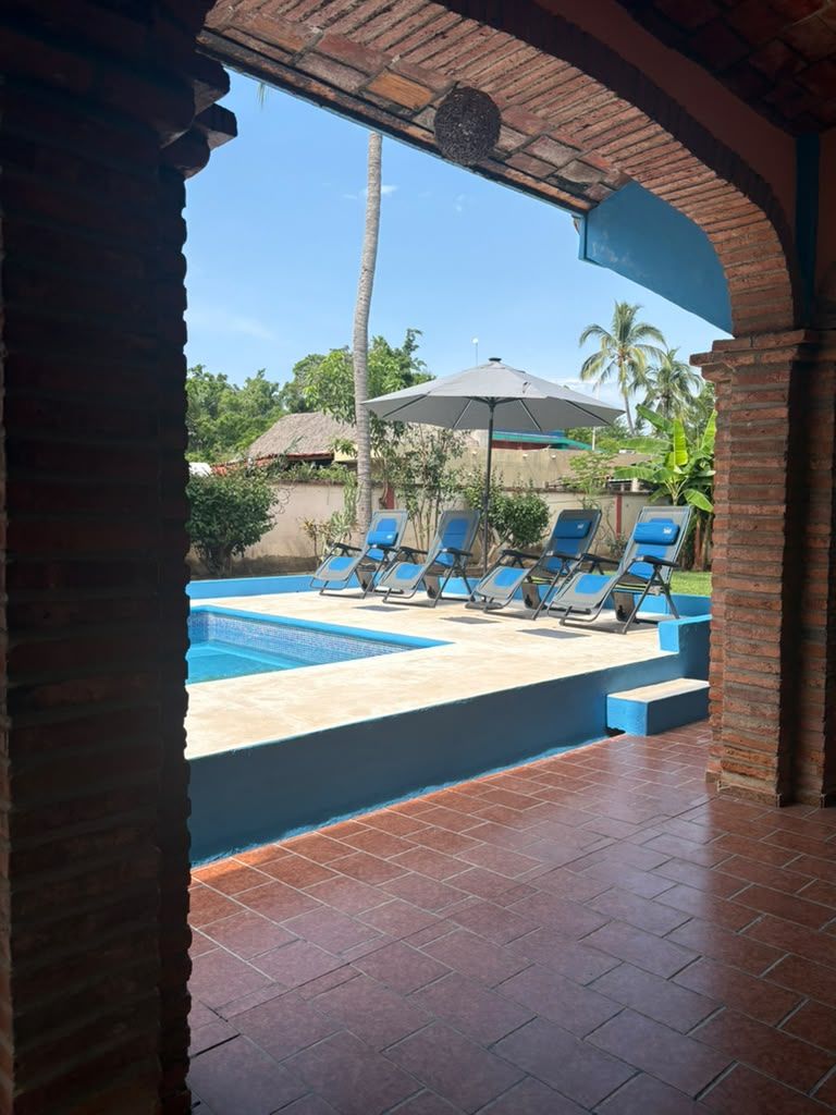 Un área de piscina con suelo de baldosas, un arco de ladrillo y sillones de descanso.