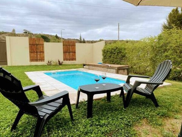 A backyard with a swimming pool, two chairs, and a table. - Cozy cabin in charming Las Compuertas, Mendoza, Argentina with Pool,AC,WiFi, (LAS COMPUERTAS)