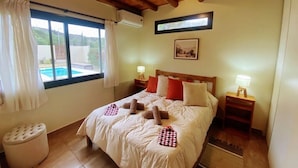 Ein Schlafzimmer mit Holzboden, einem großen Bett mit weißer Bettwäsche, roten und beigen Kissen sowie einem kleinen Nachttisch mit Lampe.