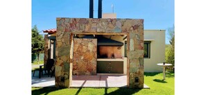 A stone-built outdoor kitchen area with a built-in grill, a seating bench, and a small table. - Cozy cabin in charming Las Compuertas, Mendoza, Argentina with Pool,AC,WiFi, (LAS COMPUERTAS)