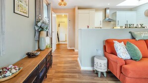 A modern living space with a sofa, a small ottoman, a wooden table, and a kitchen area in the background. - 1 bedroom accommodation in Coleford (Coleford)