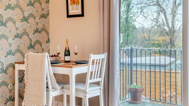A dining area with a table set for two, a bottle of champagne, and a framed picture on the wall. - 1 bedroom accommodation in Coleford (Coleford)